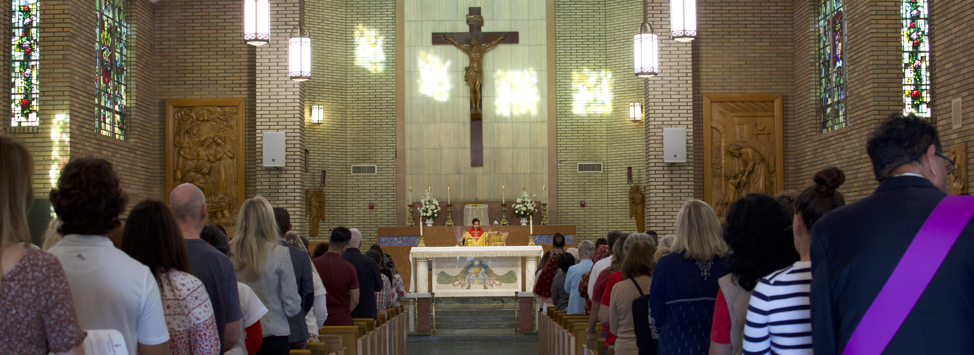 Mass at Saint Joseph's Chapel. A priest in red stands behind the altar performing the Consecration.
