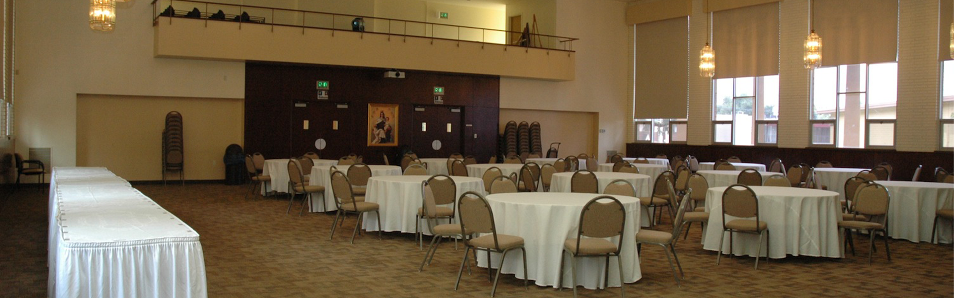 Madonna Hall set up with circular tables with white table cloth, chairs around each one. Rectangle tables, also with white table cloth, stand to the side.